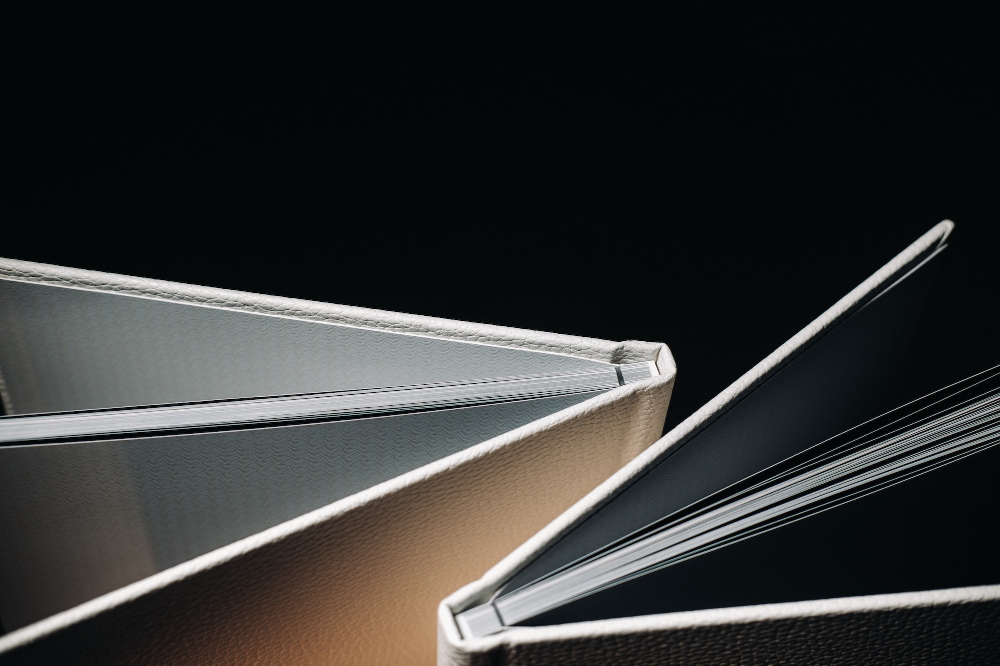 Composition of photo books in natural white leather of different sizes. The white paper on a dark